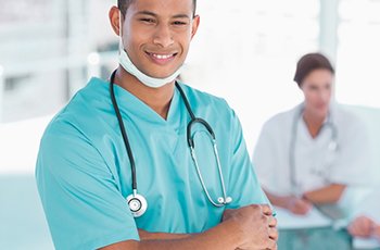 Smiling male surgeon standing with group around table in background at hospital